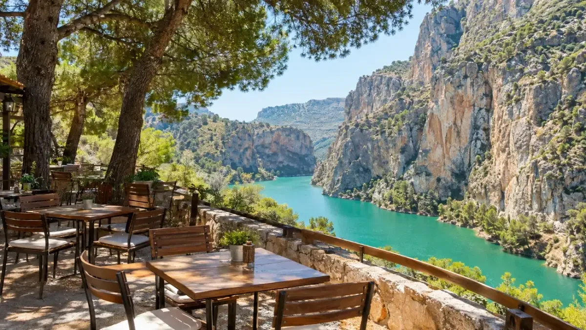 A restaurant terrace by a turquoise reservoir with pine trees