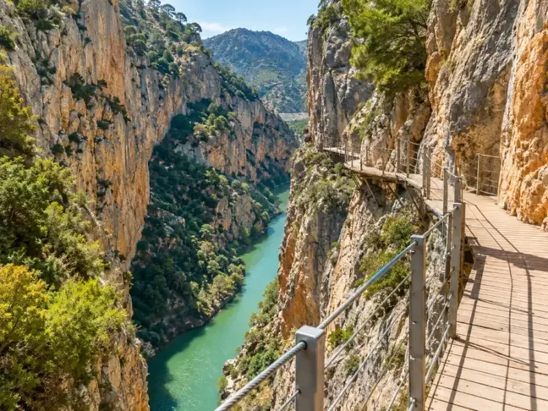 A wooden boardwalk with railings bolted to a sheer limestone cliff high above a river
