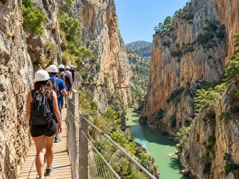 Walkers in helmets seen from behind on a boardwalk along a cliff face